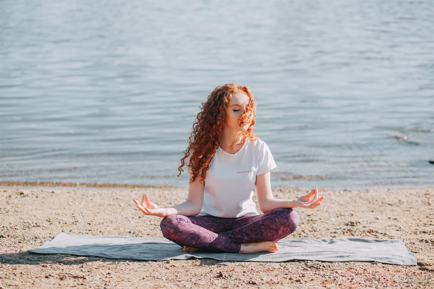 Femme assise en position de méditation sur une plage, face à la mer